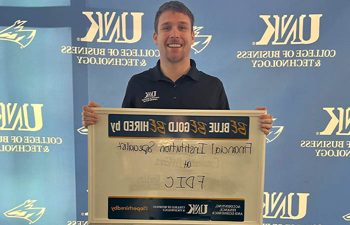 Logan Shaw holding a sign that reads, "Be Blue. Be Gold. Be Hired by Financial Institution Specialist at FDIC."